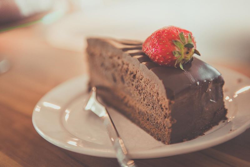 Slice of rich looking chocolate cake on a plate and topped with a strawberry.